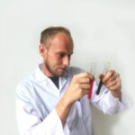 Man in a white shirt counts money, holding several banknotes against a light background.